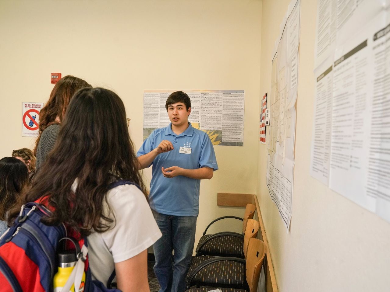 ˽̳ Davis political science major Francois Kaepellin stands in front of a wall covered in informational posters, speaking seriously to a pair of students.