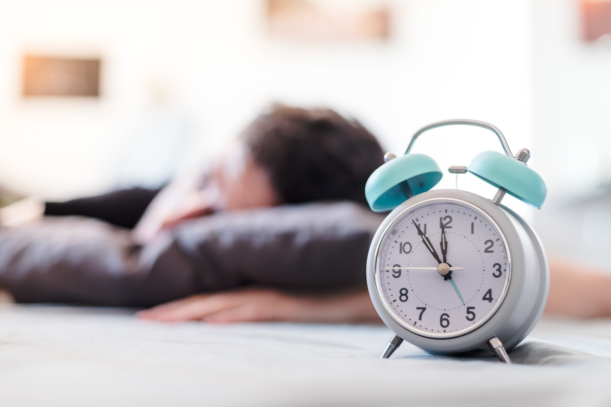 It can be tough on our bodies when we spring forward to daylight saving time. A ˽̳ Davis Health sleep expert offers strategies to help you adjust. Man shown sleeping behind the face of an alarm clock.