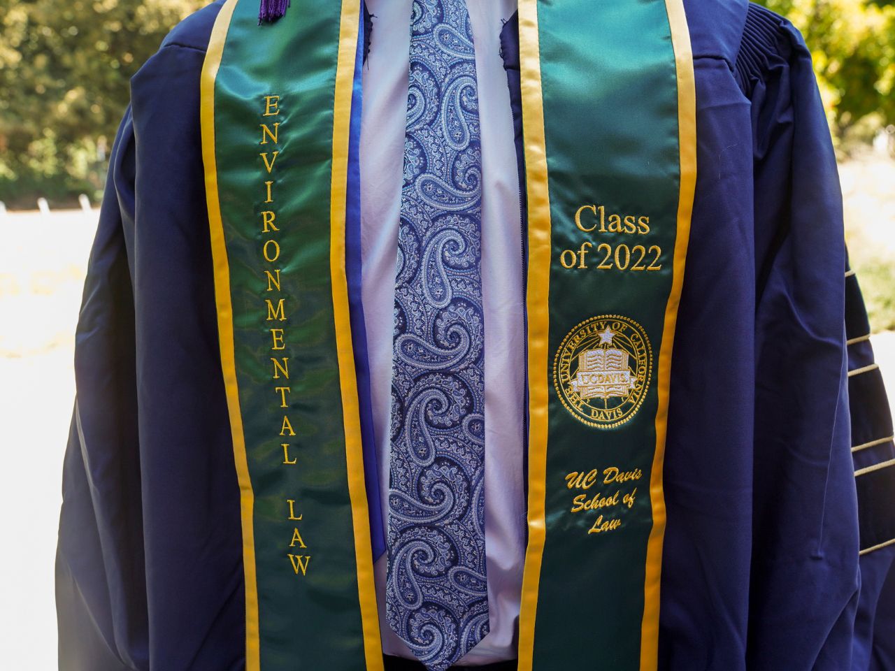 A student wearing a commencement robe and tie displays a green stole embroidered with the words "Environmental Law Class of 2022 ˽̳ Davis School of Law."