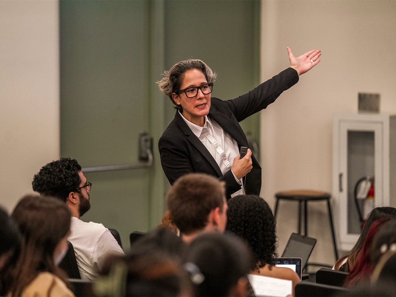 A professor with short gray hair, wearing square-rimmed glasses and a black blazer points to a presentation slide off-camera while teaching an art history class at ˽̳ Davis.