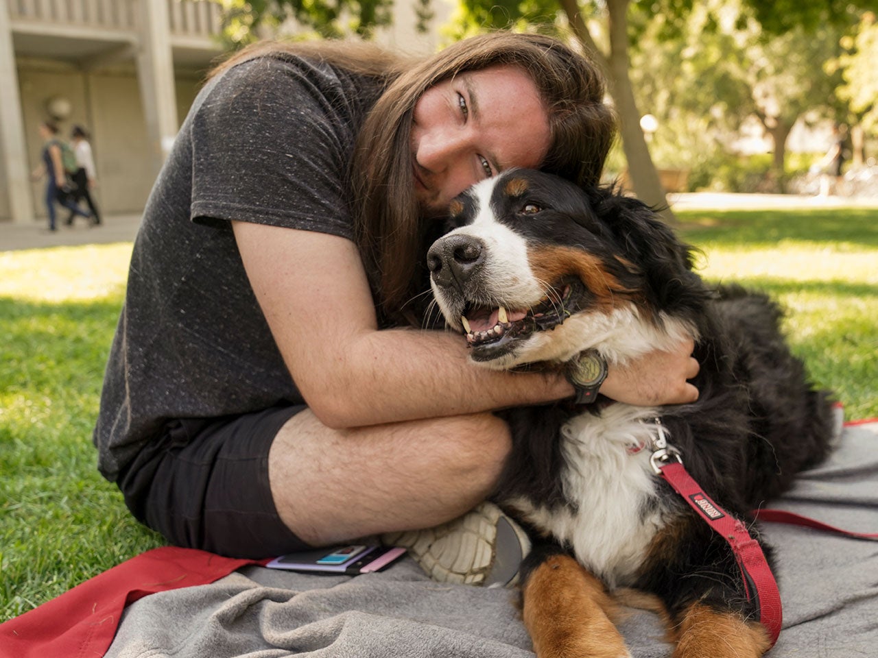 A ˽̳ Davis student sits on a blanket in the quad and hugs a large, smiling brown, black and white dog.