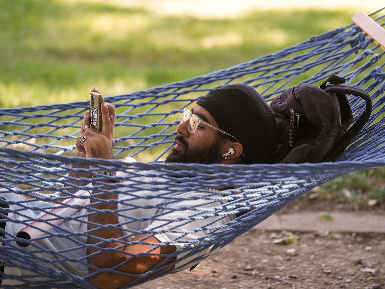 A ˽̳ Davis student scrolls on their phone while swinging in a blue hammock on campus.