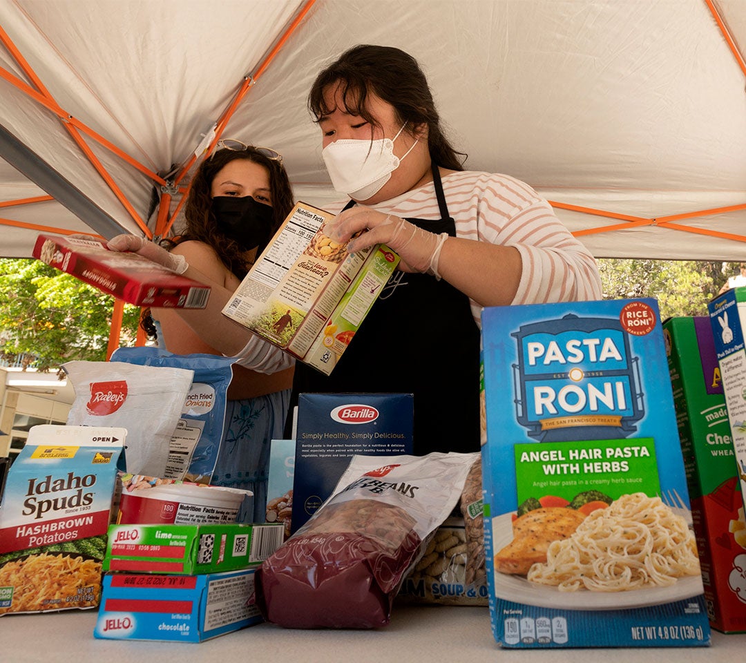 Students wearing face masks organize food items under a tent for the Eat Well Yolo program at ˽̳ Davis, aiding in community partnership and support.