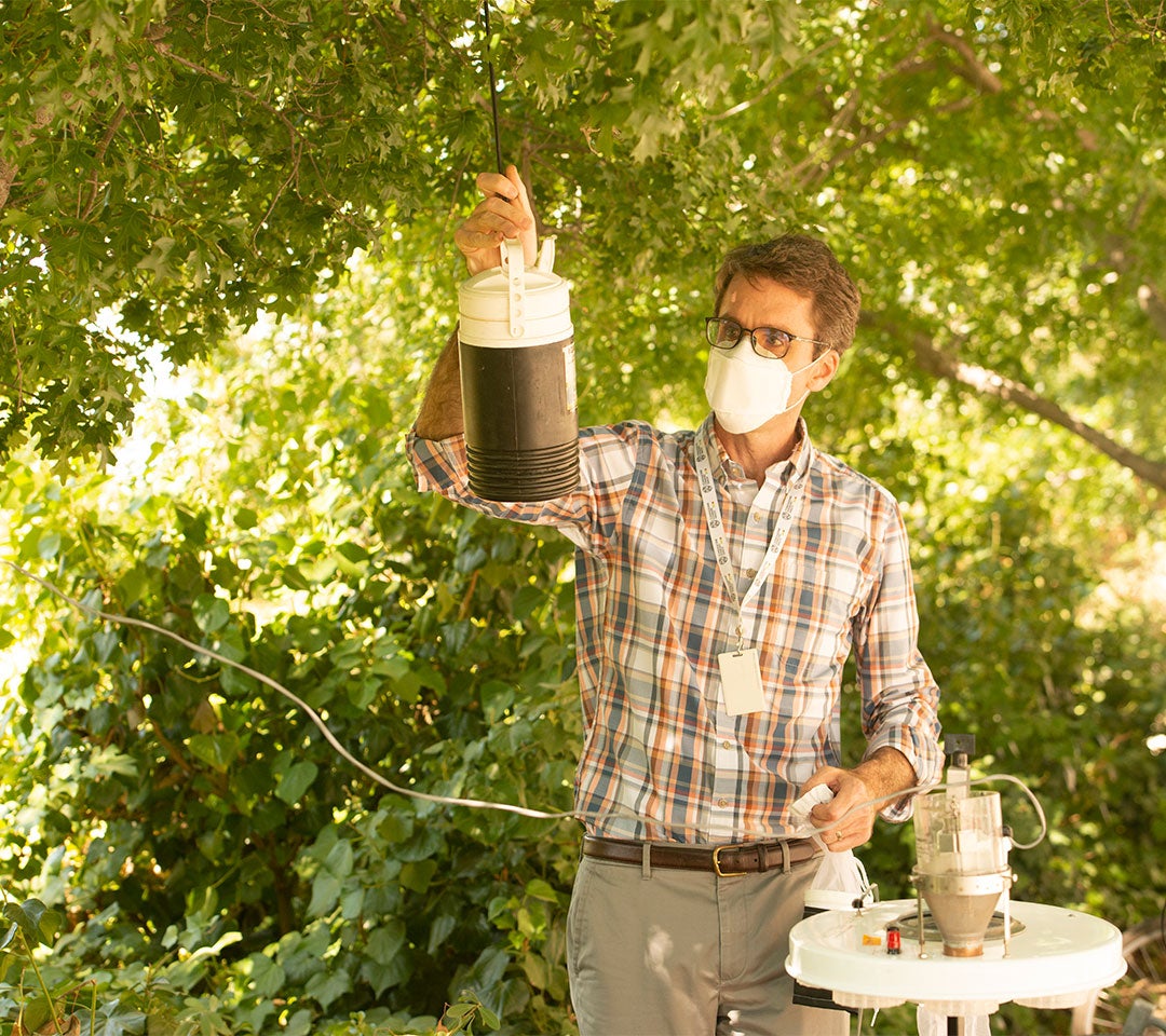 Professor Barker prepares a mosquito trap in a shaded outdoor area surrounded by greenery, contributing to ˽̳ Davis's research on mosquito-borne diseases.