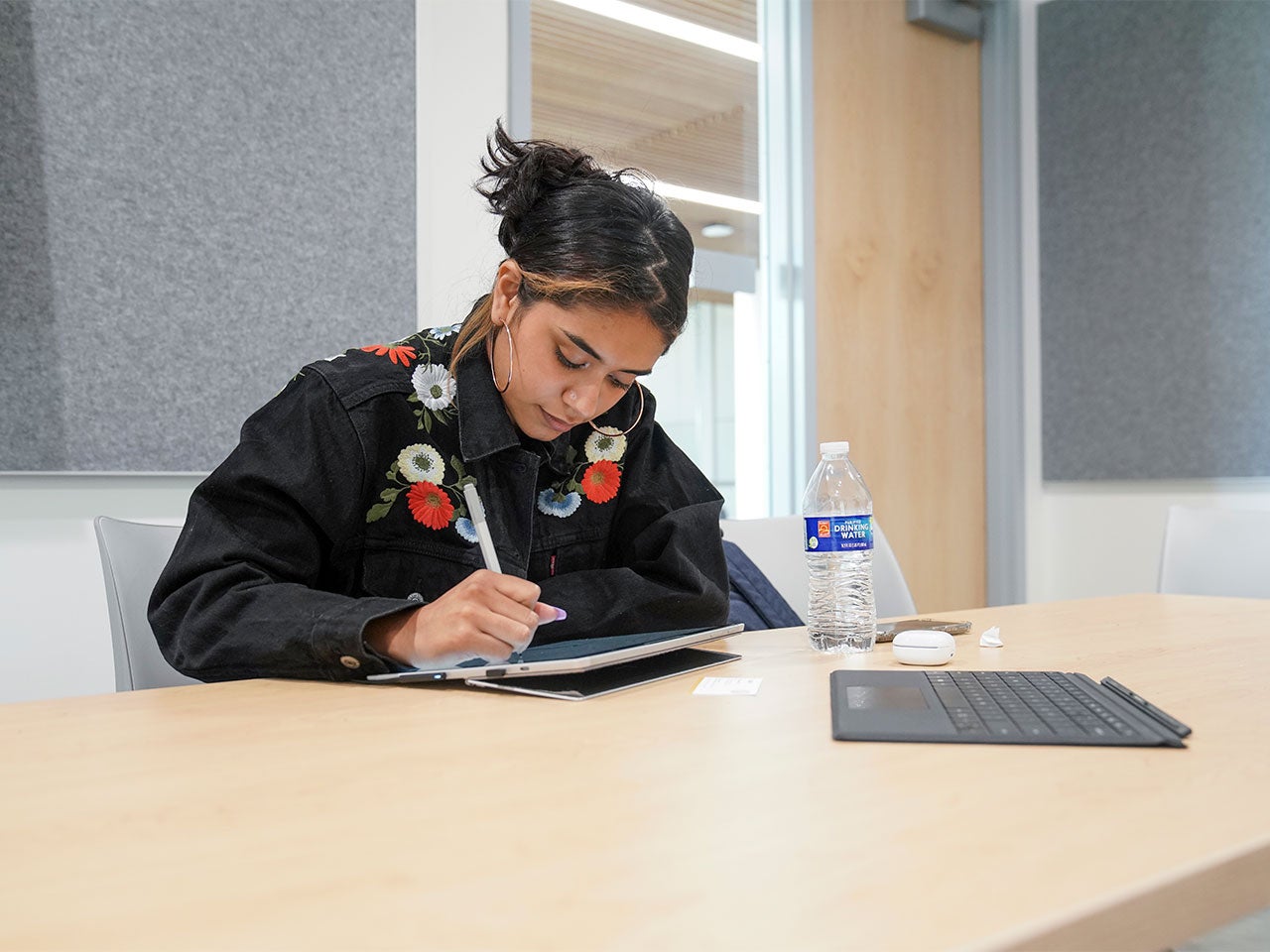 A ˽̳ Davis student, wearing hoop earrings and a black denim jacket with floral embroidery, takes notes on a tablet in ˽̳ Davis' Center for Educational Effectiveness.