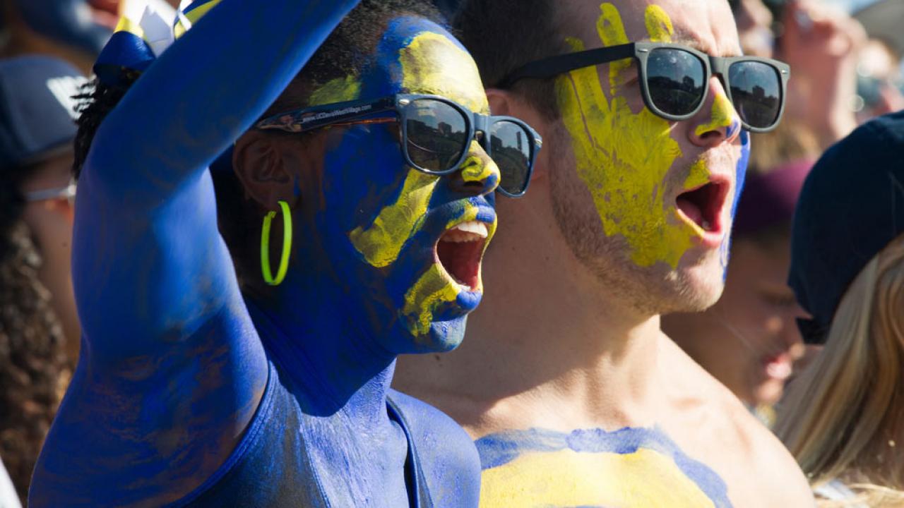 a male and female student painted in ˽̳ Davis blue and gold cheer on the Aggies at the annual homecoming football game