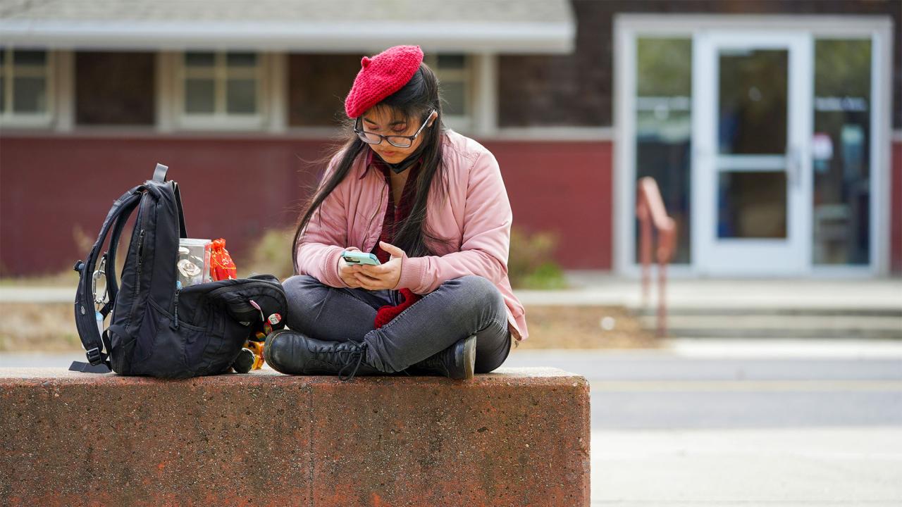 A student wearing a beret uses their smartphone outside of the ˽̳ Davis Craft Center.