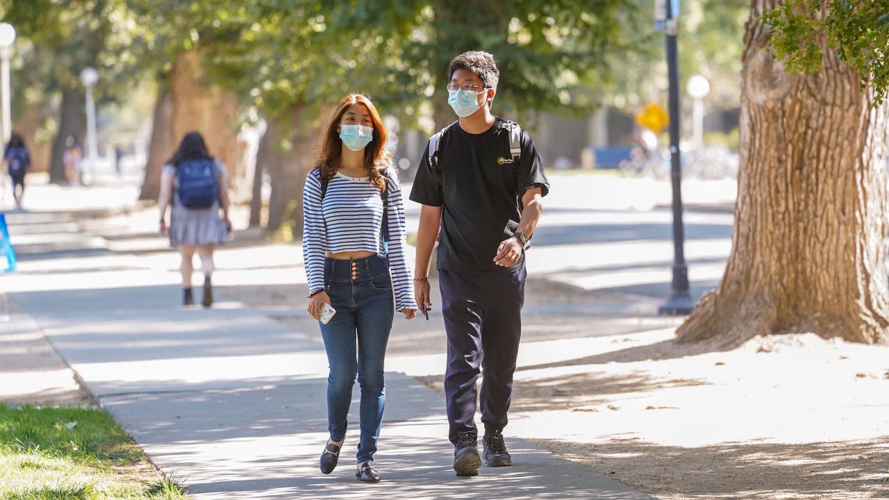 Students with masks walk through the sunlit ˽̳ Davis campus.