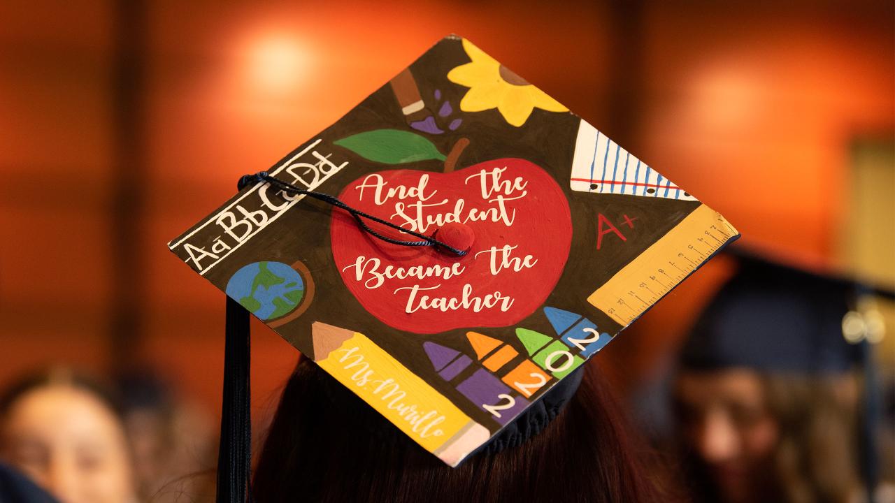 A grad cap that reads, "And the student became the teacher," in white cursive within a bright red apple, surrounded by teaching equipment like rulers, crayons and a pencil that reads, "Ms. Murillo." The photo was taken at ˽̳ Davis' School of Education Commencement graduation ceremony in 2023.
