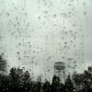 landscape of ˽̳ Davis water tower as seen through rain-splattered window on a gray day with above a silhouette of trees.