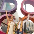 Two ˽̳ Davis students in graduation stoles in front of the colorful DOCO sculpture in downtown Sacramento.