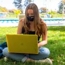 A student works on her laptop in a mask on the grass in front of a pool at ˽̳ Davis.