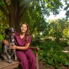 A student in scrubs poses next to a spotted dog in the leafy ˽̳ Davis Arboretum.