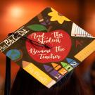 A grad cap that reads, "And the student became the teacher," in white cursive within a bright red apple, surrounded by teaching equipment like rulers, crayons and a pencil that reads, "Ms. Murillo." The photo was taken at ˽̳ Davis' School of Education Commencement graduation ceremony in 2023.